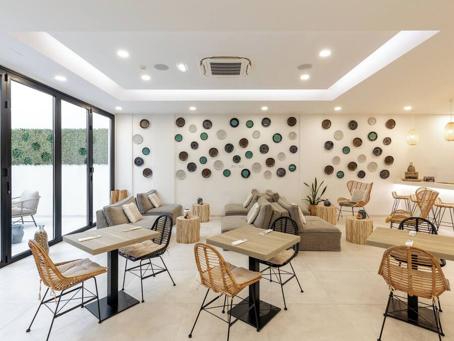A modern dining area with tables and chairs, a wall decorated with plates, and a view of the outdoors.