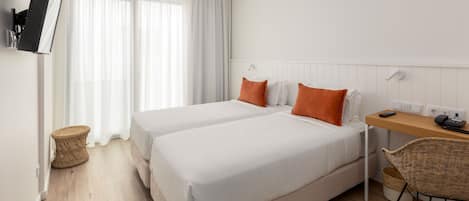 Une chambre d’hôtel avec deux lits, un bureau, une chaise, un téléviseur fixé au mur et une fenêtre avec des rideaux.