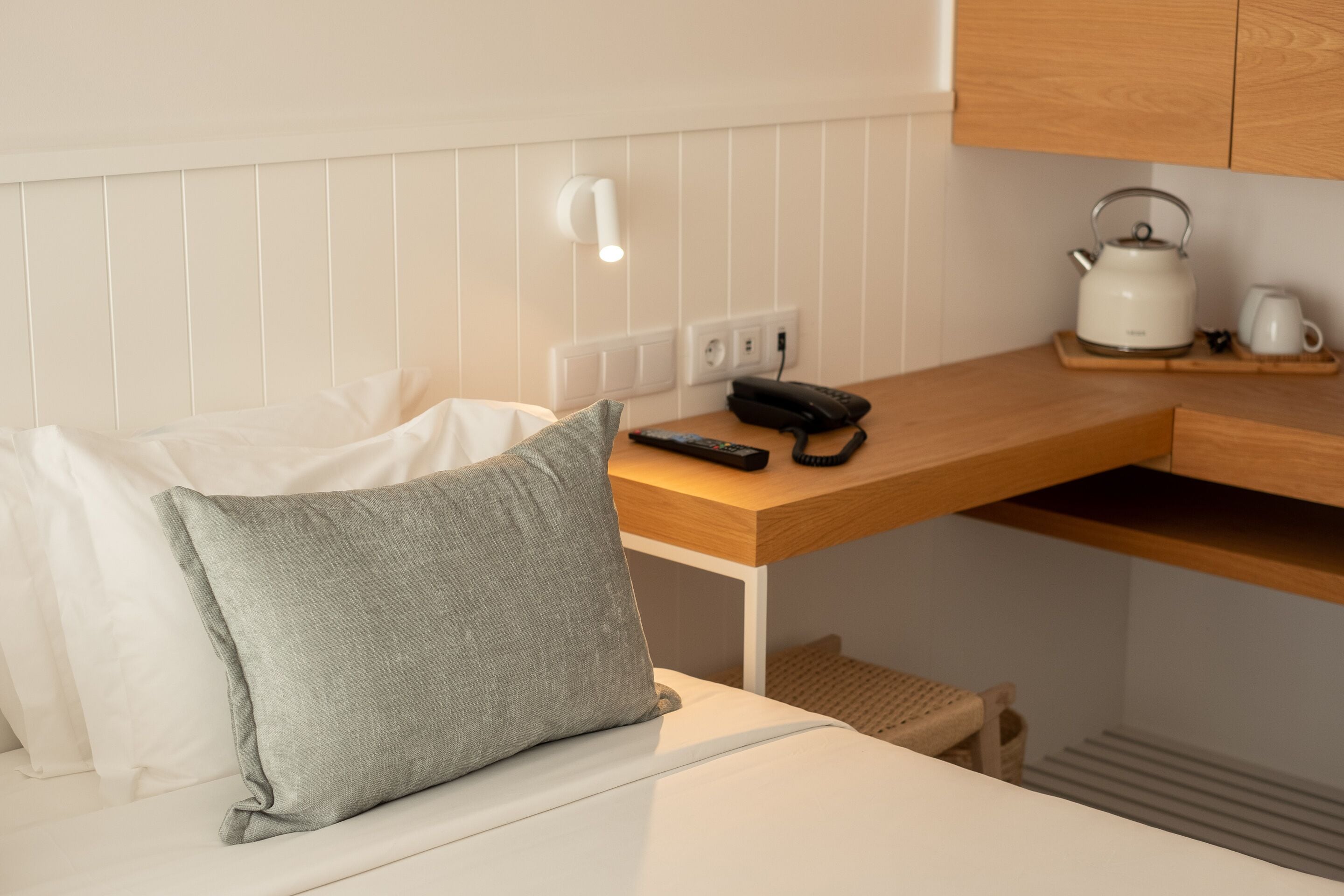 Una kitchenette compacta con una encimera blanca, un hervidor, una cafetera y un control remoto.
