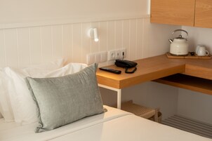 A compact kitchenette with a white countertop, a kettle, a coffee maker, and a remote control.