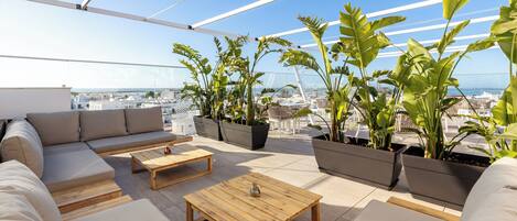 A rooftop terrace with a sofa set, wooden tables, and potted plants.