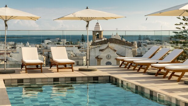 A rooftop pool area with lounge chairs and umbrellas, overlooking a coastal cityscape. - Pure Formosa Concept Hotel (Olhao)