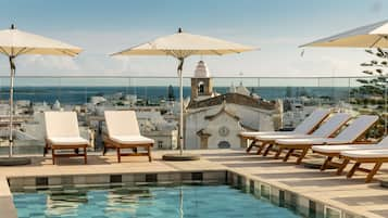 Una piscina al aire libre, sombrillas, sillones reclinables de piscina