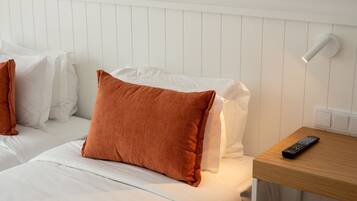 A hotel room with white bedding, a wooden nightstand, a remote control, and a wall-mounted light fixture.