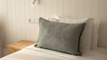 Una cama con sábanas blancas y una almohada verde.
