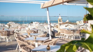An outdoor seating area with wicker chairs and tables, overlooking a coastal cityscape with buildings and a clear sky. - Pure Formosa Concept Hotel (Olhao)