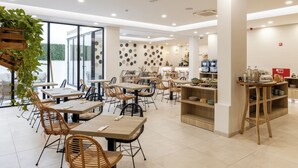 A modern cafe with wooden tables and chairs, a kitchen area, and a wall decorated with circular plates. - Pure Formosa Concept Hotel (Olhao)