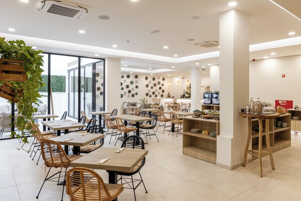A modern cafe with wooden tables and chairs, a kitchen area, and a wall decorated with circular plates. - Pure Formosa Concept Hotel (Olhao)