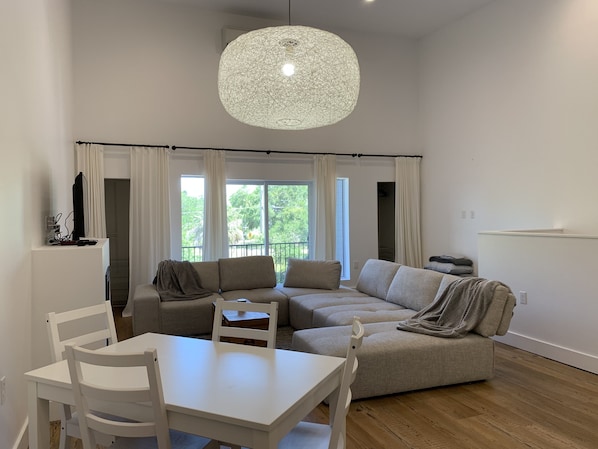 Un salón espacioso con una mesa de comedor blanca y sillas, un sofá grande color beige y una lámpara colgante.