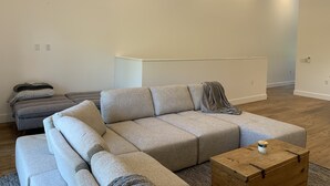 A modern living room with a large L-shaped sectional sofa, a small wooden coffee table, and a neutral color palette. - Sunset Limited: two blocks to the beach. Sleeps 2 (Bay St. Louis)