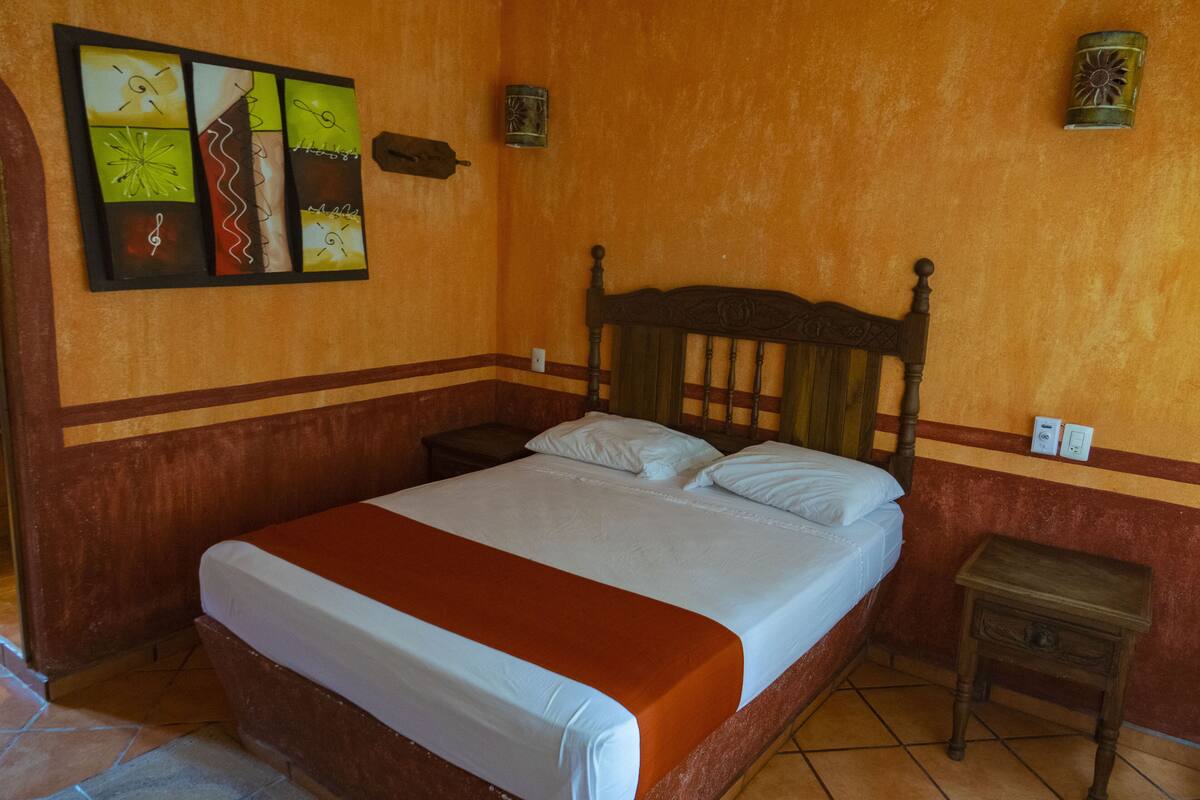 Un dormitorio con una cama grande, una mesita de noche, un reloj de pared y una obra de arte enmarcada.