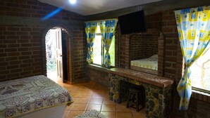 Quarto com uma cama, um banco de pedra, uma TV na parede e uma janela com cortinas.