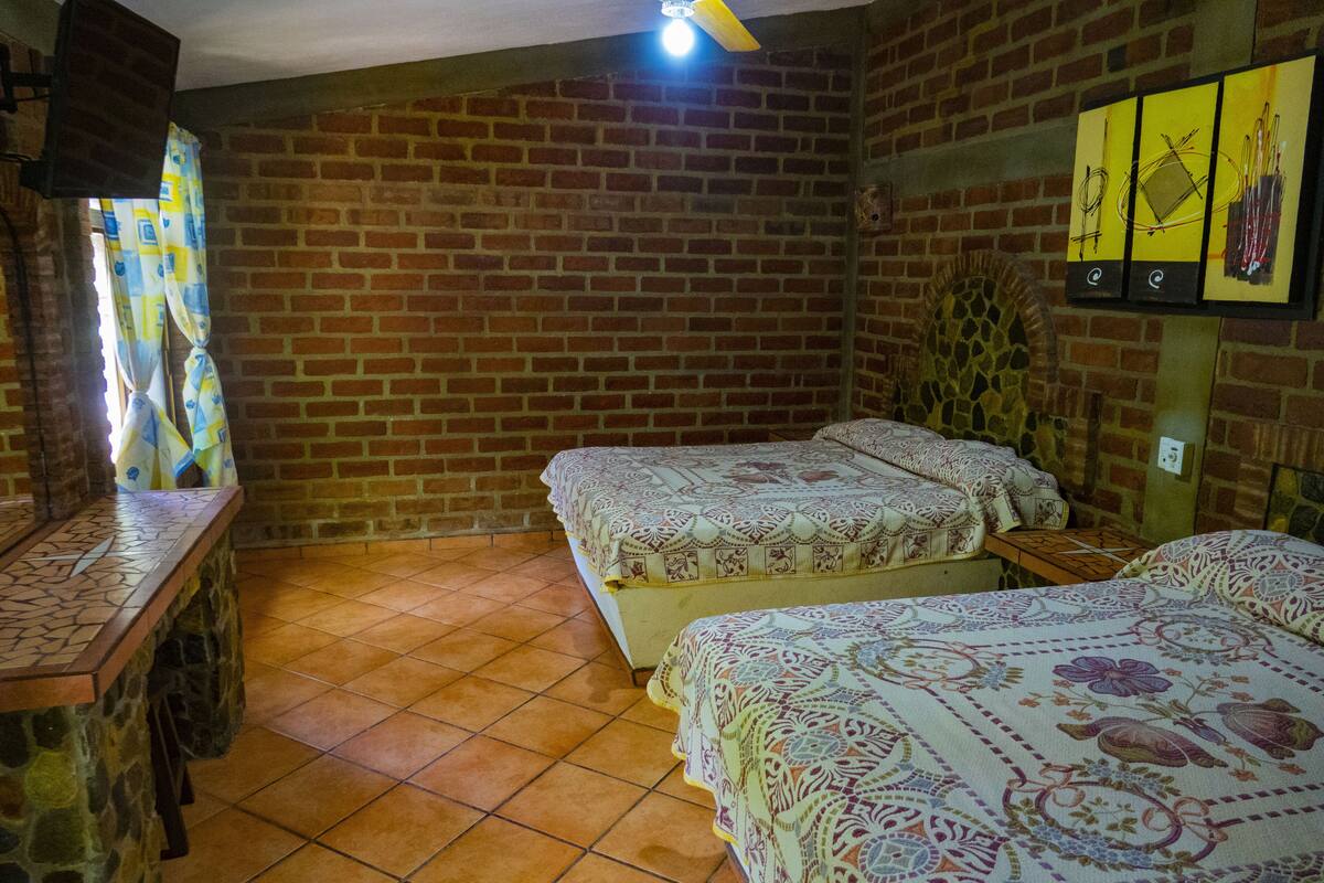 Una habitación con paredes de ladrillo, dos camas con ropa de cama estampada, una mesita y un armario de pared.