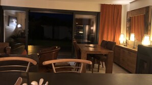 Un salon moderne avec un coin repas, de grandes portes-fenêtres coulissantes donnant sur une terrasse et une vue sur l’extérieur.