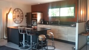 Une cuisine moderne dotée d’un îlot central, de tabourets de bar, d’une grande horloge et d’une fenêtre laissant entrer la lumière naturelle.