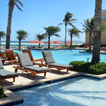 A pool area with lounge chairs, palm trees, and a view of the ocean.