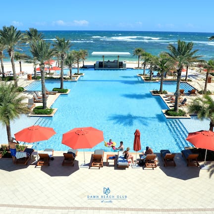 A pool area with lounge chairs and umbrellas, overlooking the ocean.