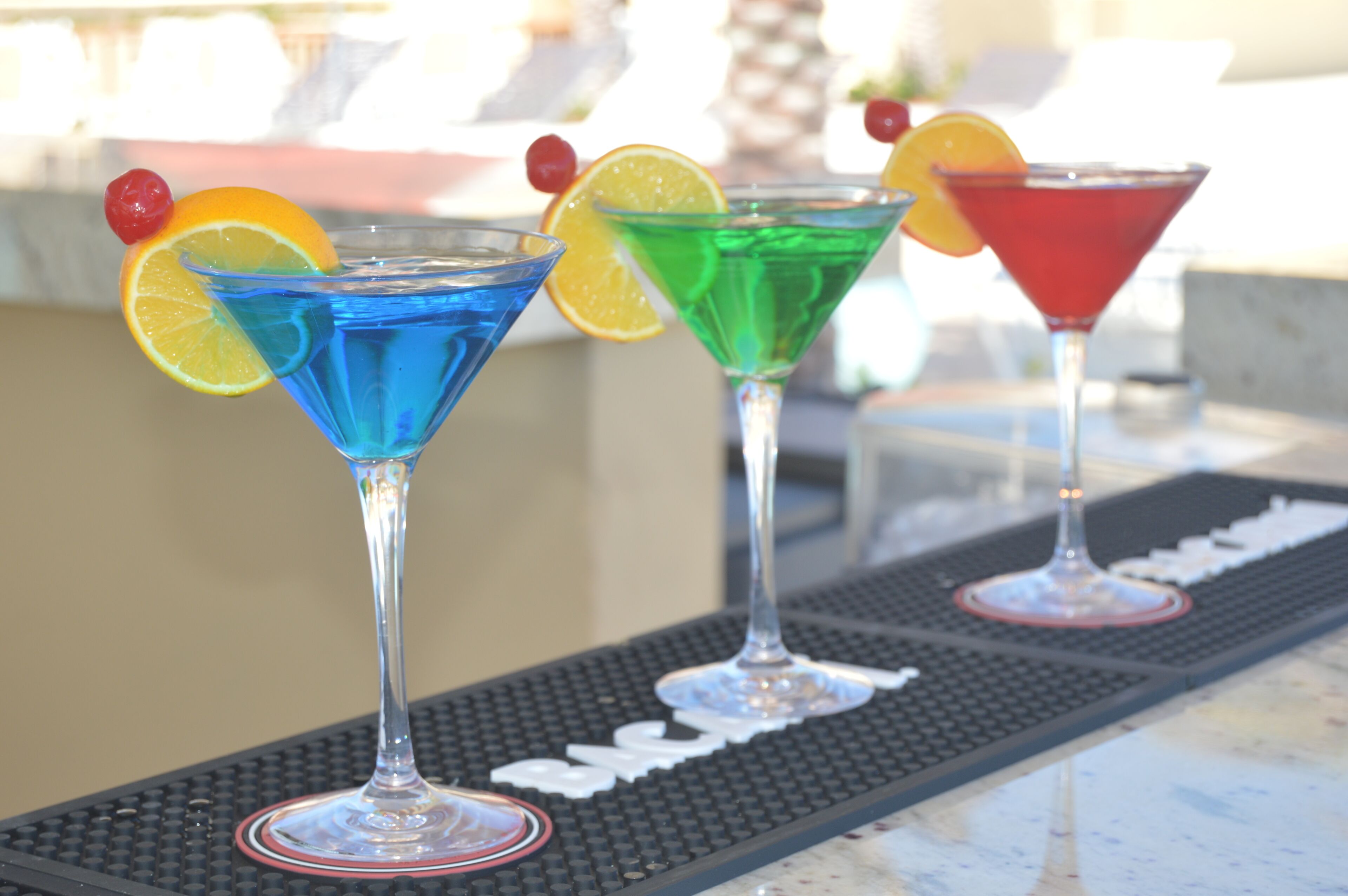 Three martini glasses with colorful drinks and garnishes on a bar mat.