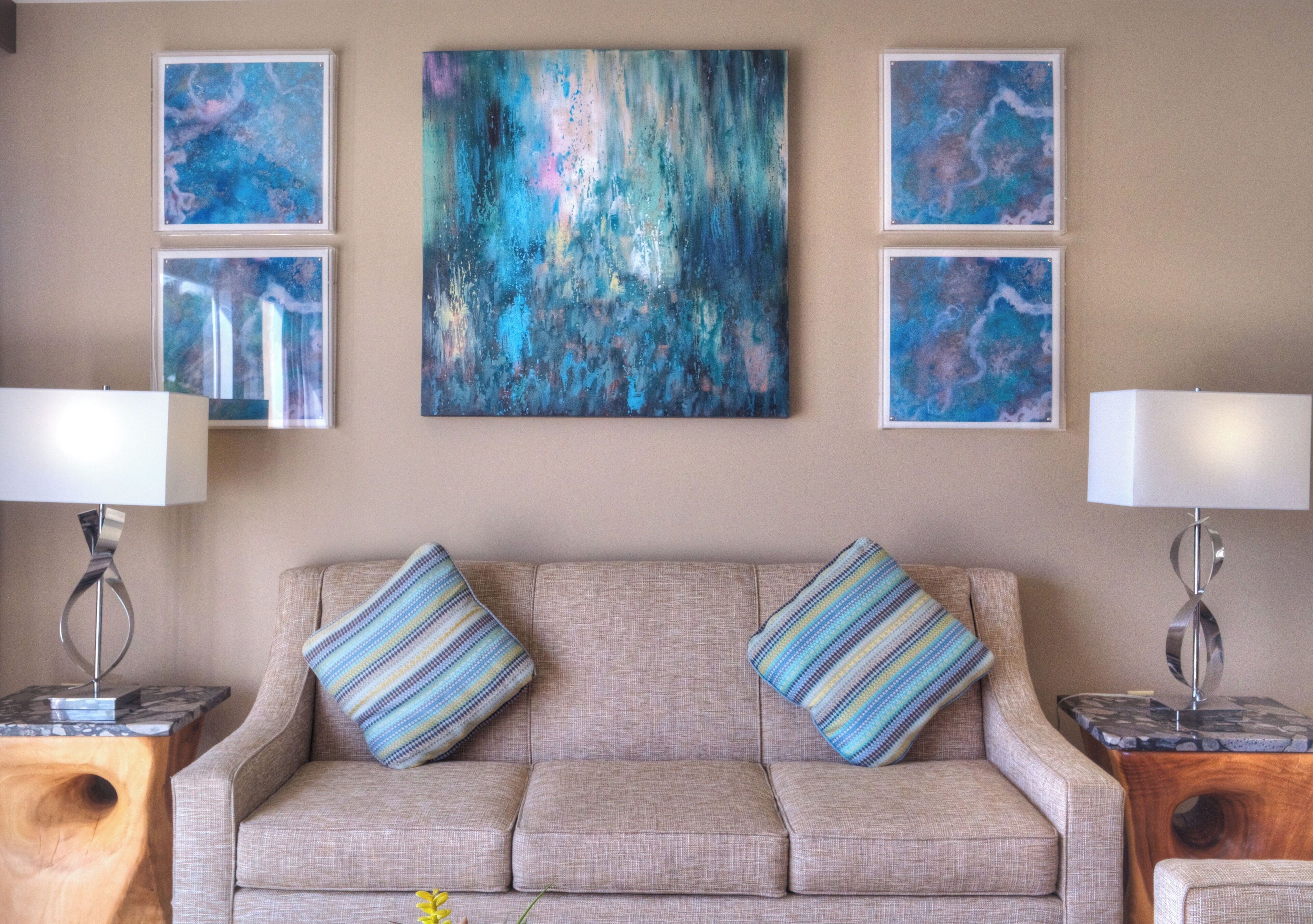 Un salón con un sofá color crema, dos cojines a rayas y un cuadro abstracto grande en la pared.