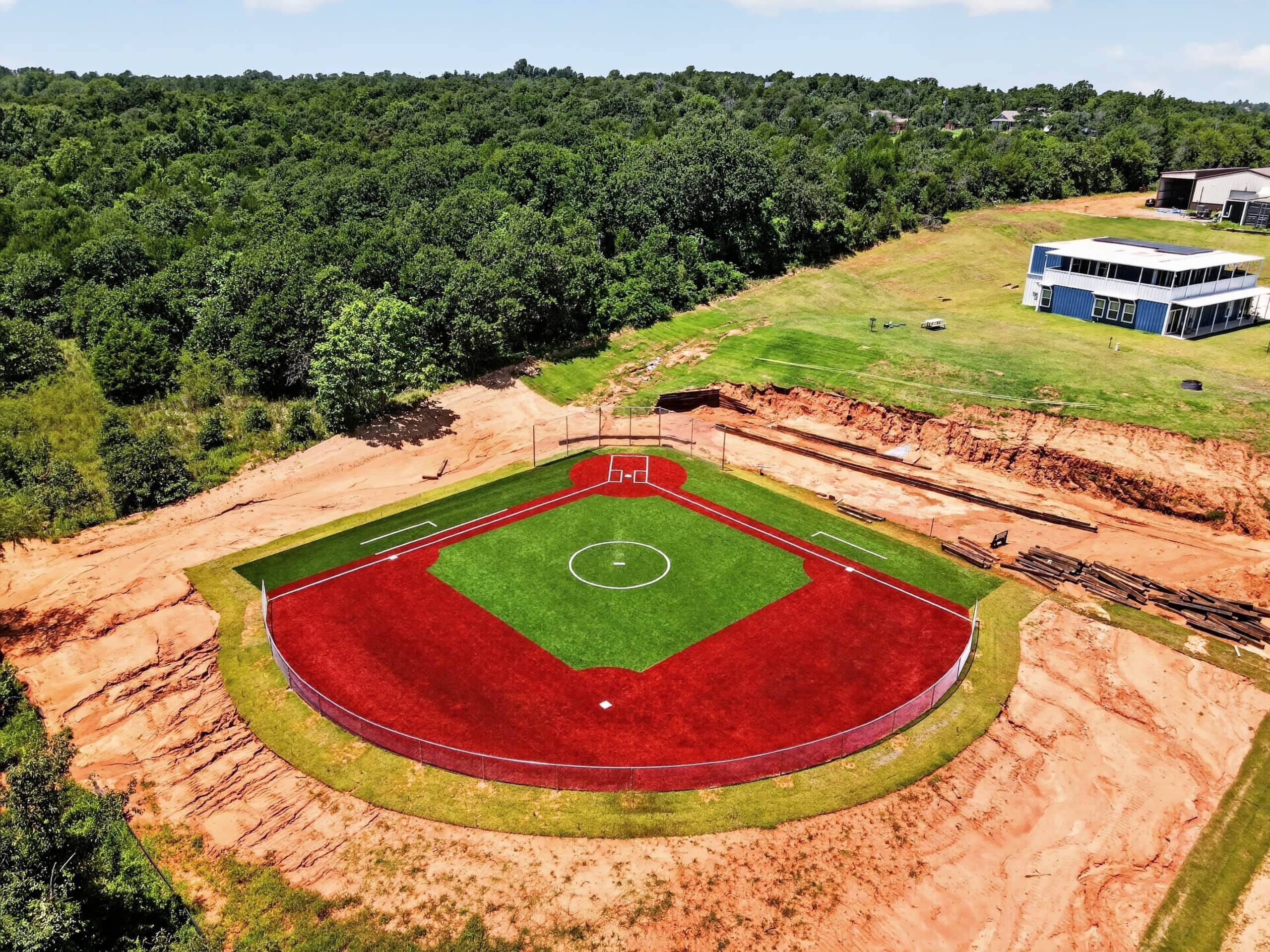 En baseballbane med en jordbane, en grøn outfield og en blå bygning i baggrunden.