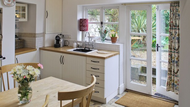 A kitchen with white cabinets, a wooden table, and a window with a view of greenery. - Fantastic character cottage, brimming with charm and set in mature gardens. (Methwold, near Thetford)