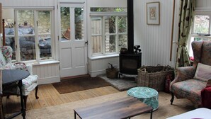 A cozy room with a fireplace, a table, a chair, and a window overlooking a garden. - Fantastic character cottage, brimming with charm and set in mature gardens. (Methwold, near Thetford)
