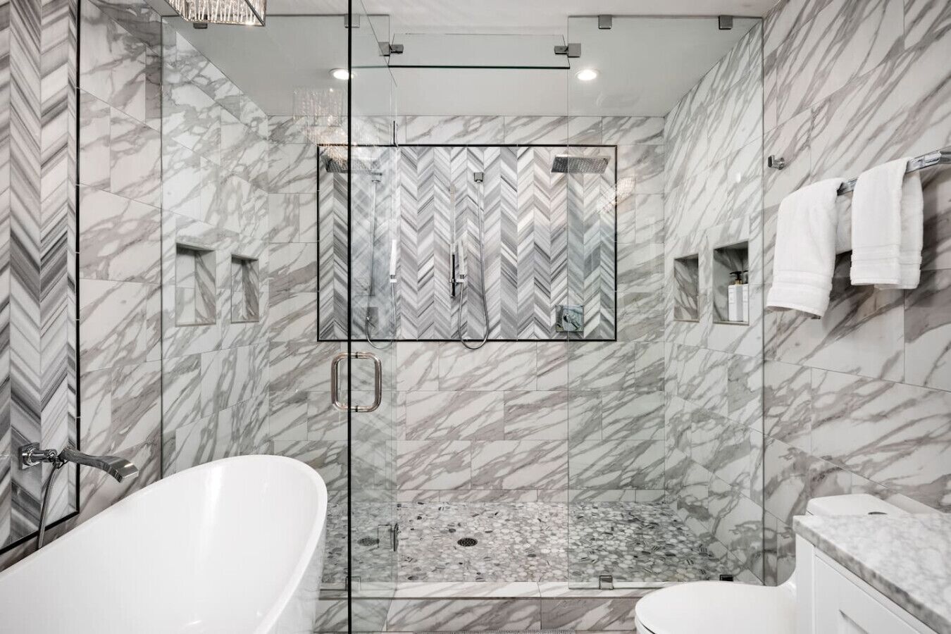 A modern bathroom with a freestanding bathtub, a glass-enclosed shower, and marble walls.