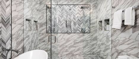 A modern bathroom with a freestanding bathtub, a glass-enclosed shower, and marble walls.