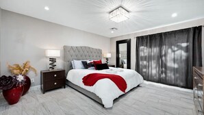 Une chambre à coucher moderne avec un grand lit, une table de chevet, un vase rouge orné de fleurs et un grand miroir.