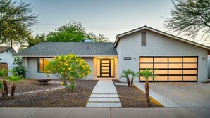 Une maison moderne avec un garage, une porte d’entrée et un petit arbre aux fleurs jaunes.