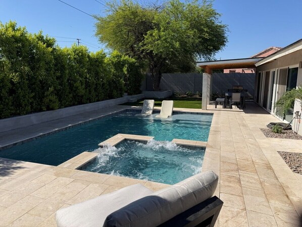 A swimming pool with a hot tub, surrounded by a patio area with a covered seating area.