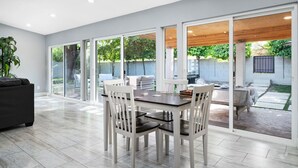 Une vaste terrasse dotée d’un espace repas, de portes-fenêtres coulissantes donnant sur un jardin, et d’un intérieur moderne agrémenté d’une grande fenêtre.