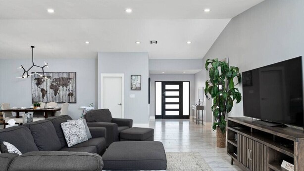 Un salon moderne avec un canapé gris, un grand téléviseur à écran plat et un coin repas comprenant une table et des chaises.