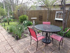 Eine Terrasse mit rundem Tisch und roten Stühlen, umgeben von einem Garten mit verschiedenen Pflanzen und einem Holzzaun.