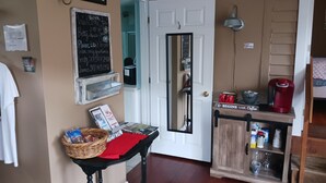 A room with a door, a wall-mounted lamp, a chalkboard with writing, a basket on a table, and a cabinet with items. - Betty Lou's Garden Guest Suite (Nashville)