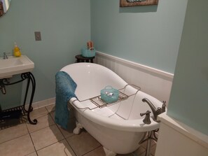Ein Badezimmer mit einer weißen Badewanne auf Füßen, einem Waschbecken und einem kleinen Hocker mit Korb.
