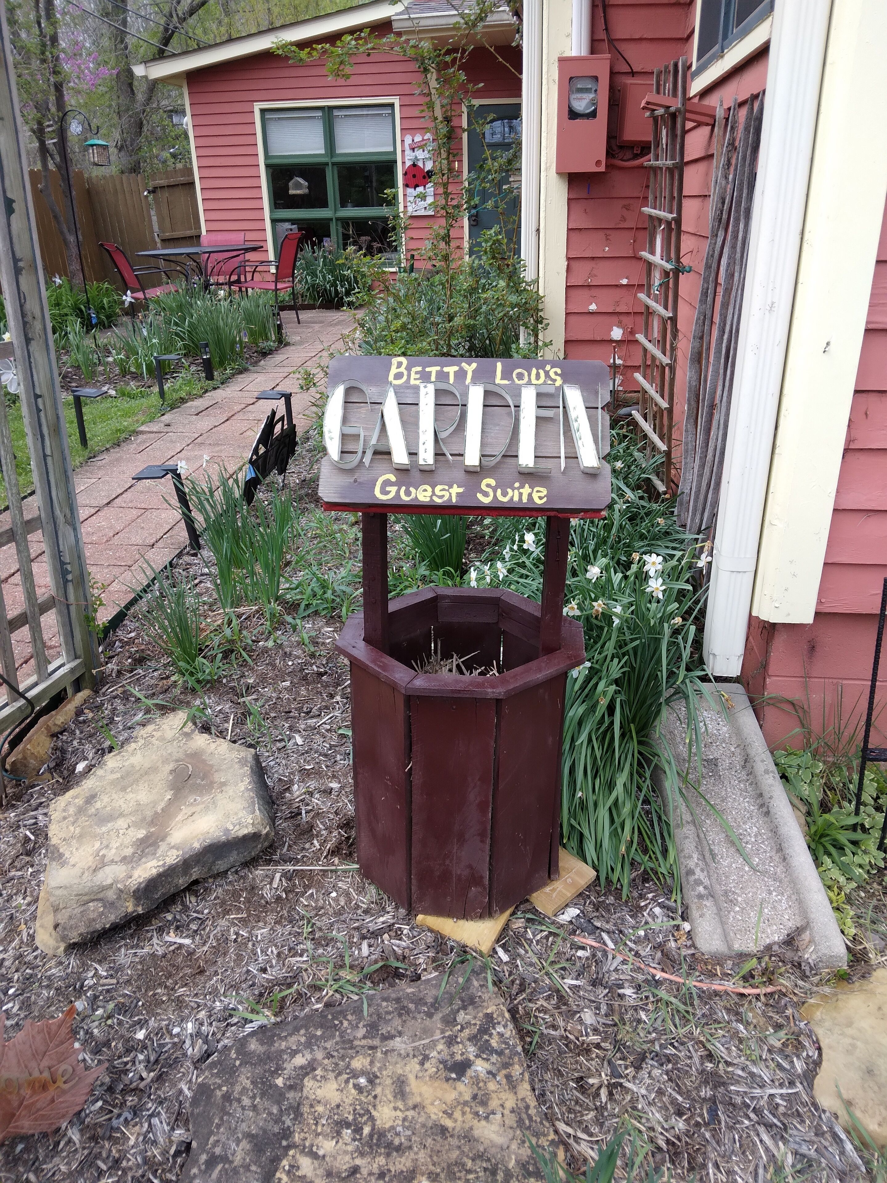 Ein Holzschild für Betty Lou's Garden Guest Suite, umgeben von Blumenbeeten und einem Holzzaun.