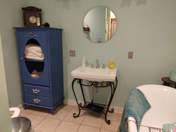 Un baño con un mueble azul, un lavabo blanco, un espejo redondo y una bañera.