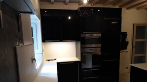 Une cuisine moderne avec des meubles noirs, un plan de travail blanc et des appareils en acier inoxydable, notamment un réfrigérateur, un four et un four à micro-ondes.