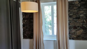 Une pièce avec un mur en pierre, une fenêtre avec des rideaux et un luminaire suspendu.