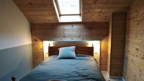 Une pièce en bois avec un lit, une lucarne et un plafond en bois.