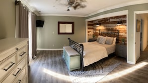 A bedroom with a bed, dresser, and a TV on the wall.