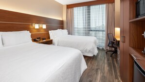 A hotel room with two beds, a desk, a chair, a TV, and a window with curtains.