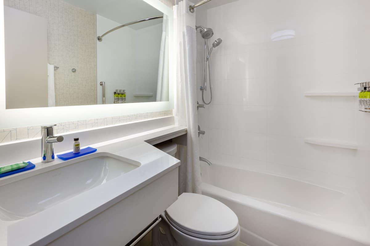 Un baño moderno con lavamanos, espejo y bañera blancos.