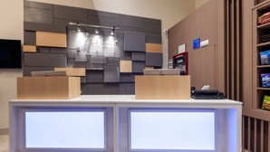 A hotel reception desk with a modern design, featuring a flat-screen TV, a digital display, and a nameplate.
