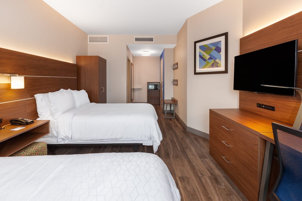 Habitación de hotel con dos camas, un escritorio, un televisor y un armario.
