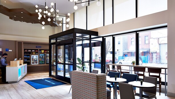 A modern lobby with a reception desk, seating area, and large windows offering a view of the street.