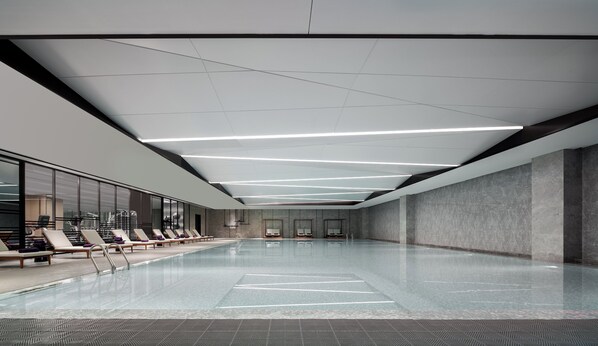 Une piscine intérieure moderne, dotée d’une eau cristalline, de nombreux fauteuils de relaxation et d’un plafond pourvu d’un système d’éclairage linéaire.