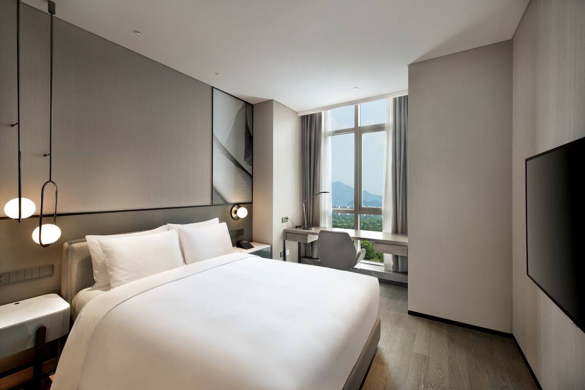 A modern hotel room with a large bed, a desk, and a TV.