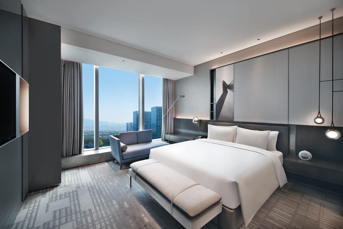 Quarto de hotel moderno com uma cama grande, um espaço para sentar e vista para a cidade.